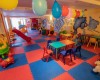 Sala zabaw dla dzieci z kolorowymi stołami, krzesłami, zjeżdżalnią i nadmuchanymi balonami.
