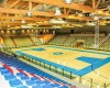 Wnętrze hali sportowej z boiskiem do koszykówki i pustymi trybunami.