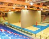 Wnętrze hali sportowej z niebieskimi siedzeniami i wielofunkcyjnym boiskiem podzielonym przegrodą.
