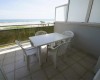 Balkon z widokiem na plażę i morze, wyposażony w cztery białe plastikowe krzesła i stół.