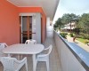 Balkon z białym plastikowym stołem i krzesłami obok pomarańczowej ściany z widokiem na zieleń.
