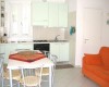Mała kuchnia z białym blatem, stół jadalniany z krzesłami i pomarańczowa kanapa.