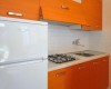 Kuchnia z pomarańczowymi szafkami, białą lodówką i kuchenką gazową.