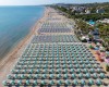 Rzędy białych i niebieskich parasoli na długiej piaszczystej plaży nad morzem.