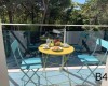 Dwa niebieskie krzesła i żółty stół ze śniadaniem na balkonie z widokiem na las.