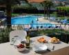 Stół z jedzeniem z widokiem na odkryty basen otoczony leżakami i palmami.