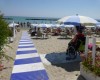 Osoba na wózku inwalidzkim na piaszczystej plaży z rampą i parasolami.