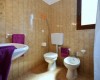Łazienka z umywalką, toaletą i bidetem, wyposażona w fioletowe ręczniki.