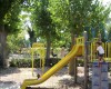 Plac zabaw z zjeżdżalnią i huśtawkami otoczony drzewami.