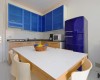 Kuchnia z niebieskimi szafkami, stołem i fioletową lodówką.