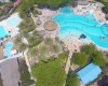 Widok z lotu ptaka na rozległy aquapark z basenami i palmami otoczony zielenią.