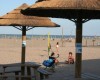 Plaża z drewnianymi altanami i ludźmi korzystającymi z słonecznego dnia nad morzem.