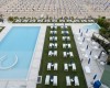 Leżaki wokół basenu obok plaży z rzędami parasoli i leżaków.  