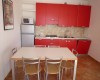 Kuchnia z czerwonymi szafkami, stołem jadalnianym i czterema krzesłami.