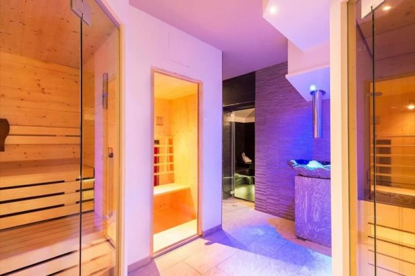 Nowoczesne spa z drewnianą sauną i kamienną ścianą oświetloną niebieskim światłem.