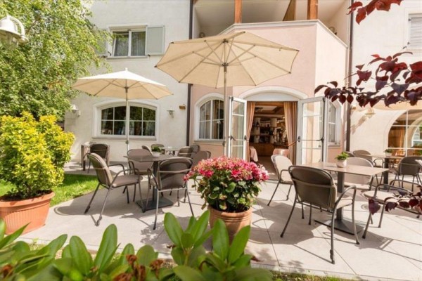 Taras z kilkoma stolikami i parasolami przed kawiarnią lub restauracją.