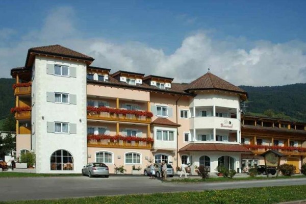 Duży trzypiętrowy hotel z żółtymi i białymi fasadami, balkonami i zaparkowanymi samochodami przed budynkiem.
