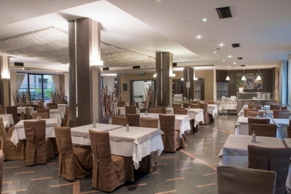 Przestronna restauracja z brązowymi krzesłami i białymi obrusami na stołach.