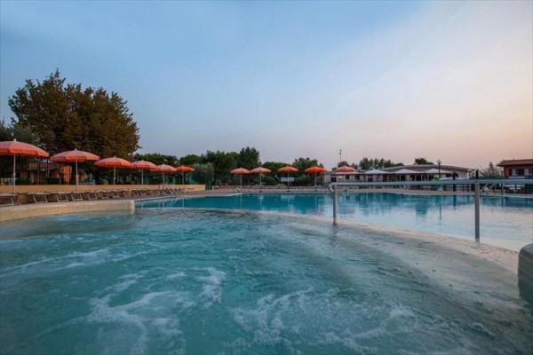 Zewnętrzny basen z jacuzzi otoczony leżakami i parasolami.