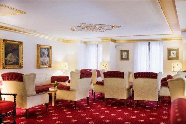 Elegancka przestrzeń wypoczynkowa z czerwonymi i kremowymi fotelami oraz obrazami na ścianach.