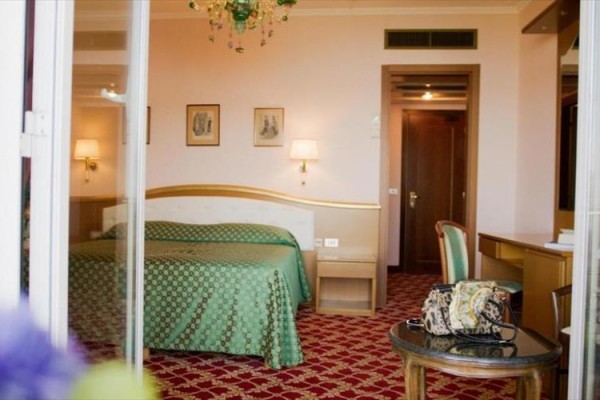 Pokój hotelowy z podwójnym łóżkiem, biurkiem i centralnym żyrandolem.