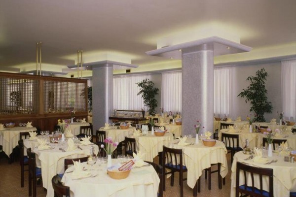 Przestronna restauracja z okrągłymi stołami nakrytymi żółtymi obrusami.