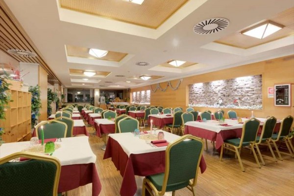 Restauracja z rzędami stołów z białymi obrusami i zielonymi krzesłami.