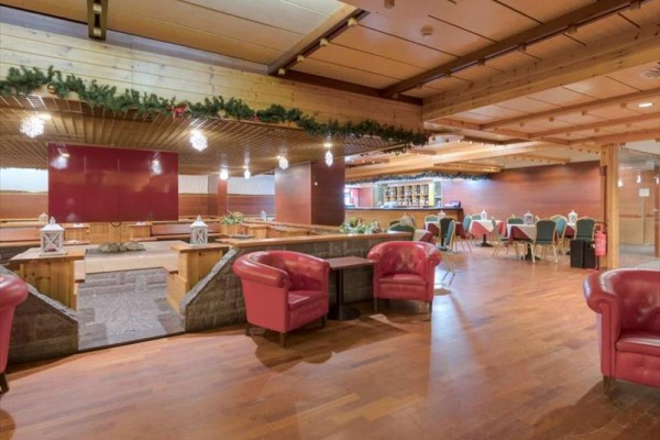 Wnętrze drewnianej restauracji z czerwonymi fotelami, dekoracja świąteczna i bar.