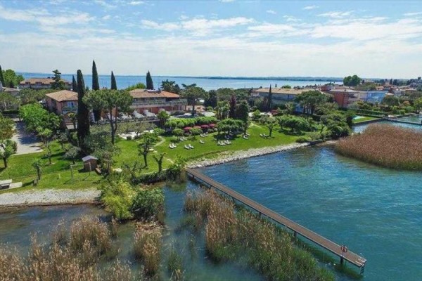 Widok na zielony park z budynkami nad jeziorem i drewnianym pomostem.
