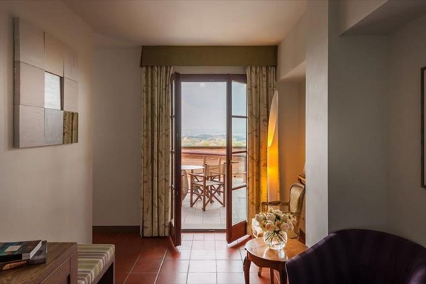 Otwarte drzwi prowadzące z pokoju na balkon z widokiem na krajobraz.