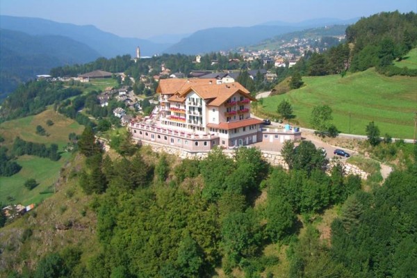 Hotel na szczycie wzgórza otoczony zielonymi łąkami i lasami.