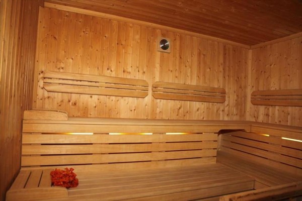 Drewniana sauna z ławkami i wiadrem z liśćmi w rogu.