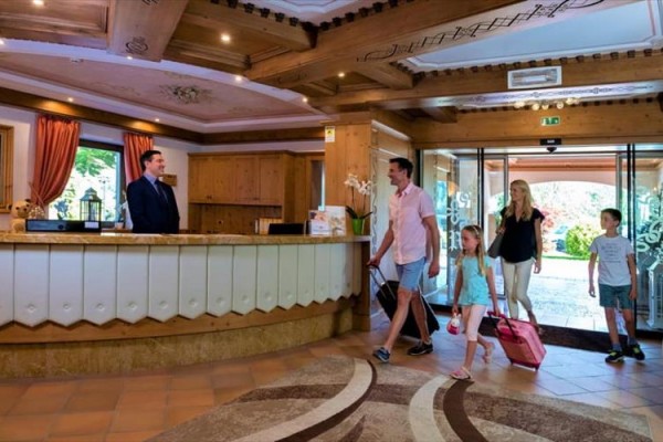 Rodzina z walizkami wchodzi do recepcji hotelu, gdzie stoi recepcjonista.