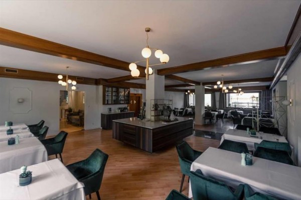 Restauracja z drewnianymi belkami, białym sufitem i krzesłami z ciemnymi pokrowcami.