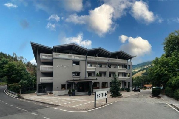 Nowoczesny szary hotel z balkonami i skośnym dachem otoczony przyrodą.