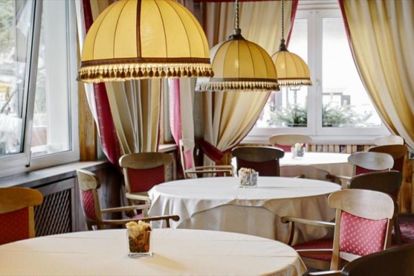 Elegancka restauracja z okrągłymi stołami, czerwonymi krzesłami i dużymi lampami z frędzlami.
