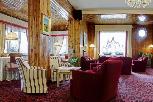 Elegancka hotelowa lounge z czerwonymi fotelami i drewnianą boazerią.
