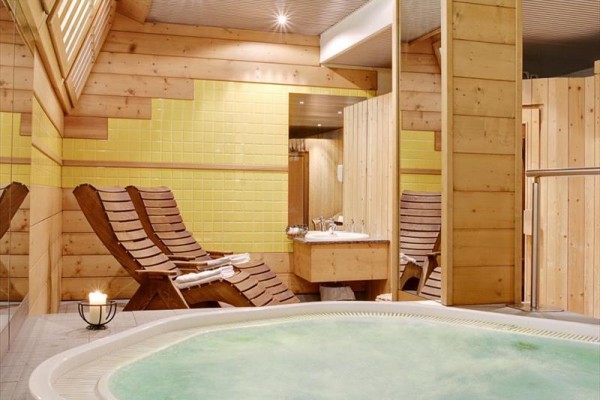Pomieszczenie wellness z jacuzzi, drewnianymi leżakami i żółtymi płytkami na ścianie.