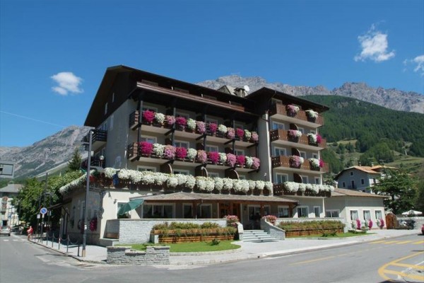 Hotel z ozdobionymi balkonami kwiatami na tle gór i lasu.
