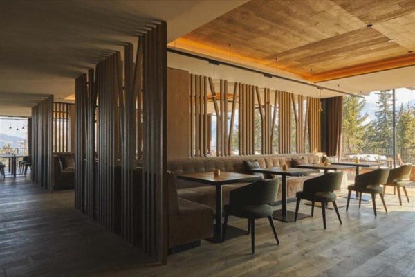 Nowoczesne wnętrze restauracji z drewnianą boazerią i dużymi oknami.