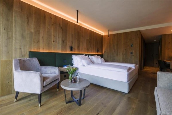 Nowoczesny pokój hotelowy z dużym łóżkiem, fotelem i drewnianymi panelami na ścianach.