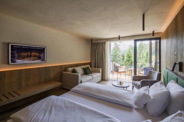 Pokój hotelowy z dużym łóżkiem, sofą i balkonem z widokiem na drzewa.