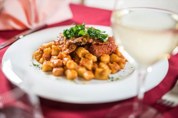 Talerz gnocchi z sosem pomidorowym i ziołami na stole z białym winem.