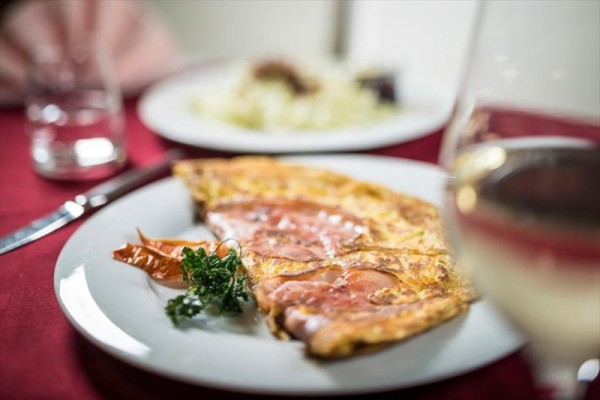 Porcja omletu z plastrami szynki na talerzu z kieliszkiem wina na pierwszym planie.