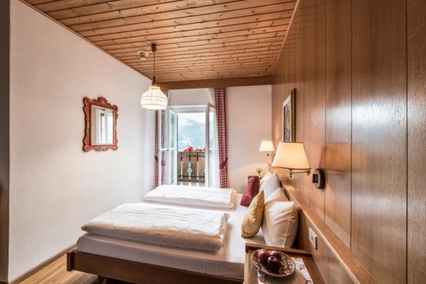Tradycyjna przytulna sypialnia z drewnianym sufitem, łóżkiem podwójnym i widokiem na balkon z górskim krajobrazem na zewnątrz.
