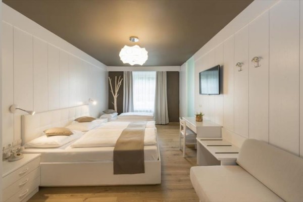 Nowoczesny pokój hotelowy z dwoma łóżkami, kanapą, biurkiem i telewizorem na ścianie.