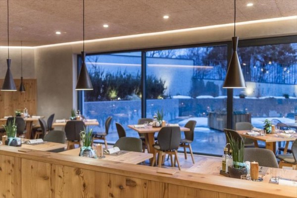 Nowoczesna restauracja z drewnianymi stołami, krzesłami i dużymi oknami z widokiem na zewnątrz.