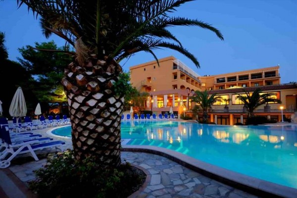 Wieczorny widok na hotel z basenem i palmami.