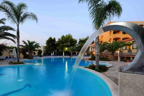 Basen przy hotelu z fontanną i palmami w tle.