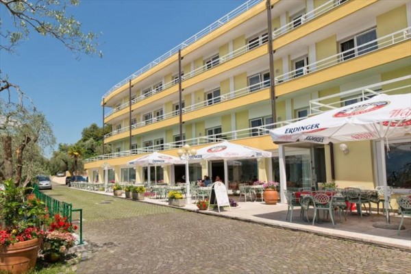 Obok trzypiętrowego hotelu stoliki i parasole na tarasie.